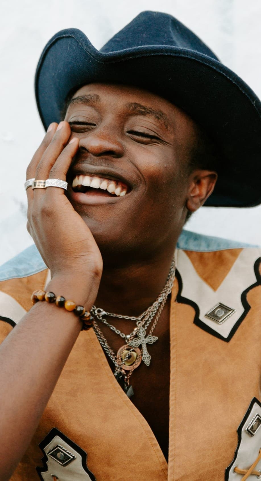 A laughing man in a wide-brimmed hat, hand on his cheek